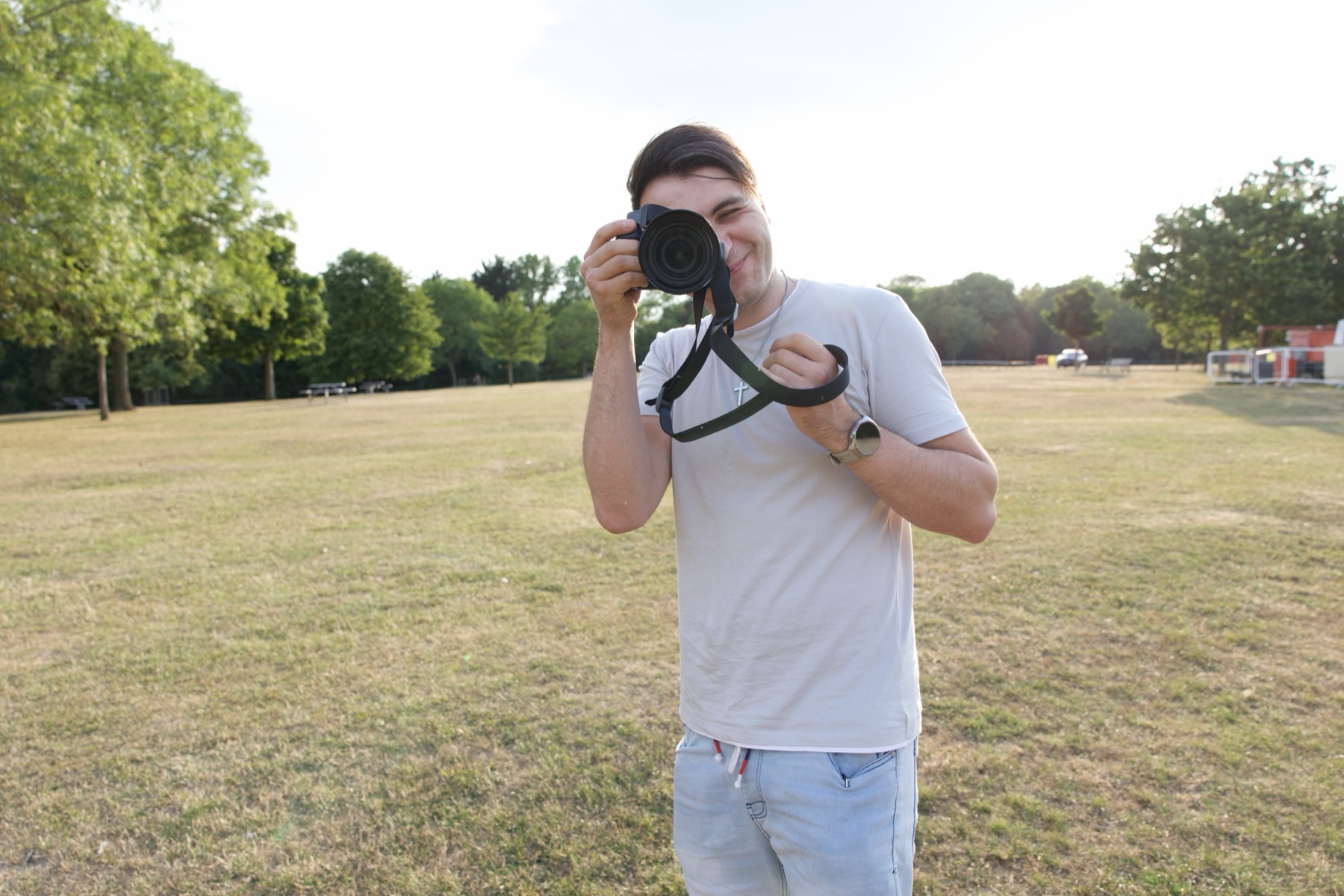 Alex holding a camera up to take a photo in an open field