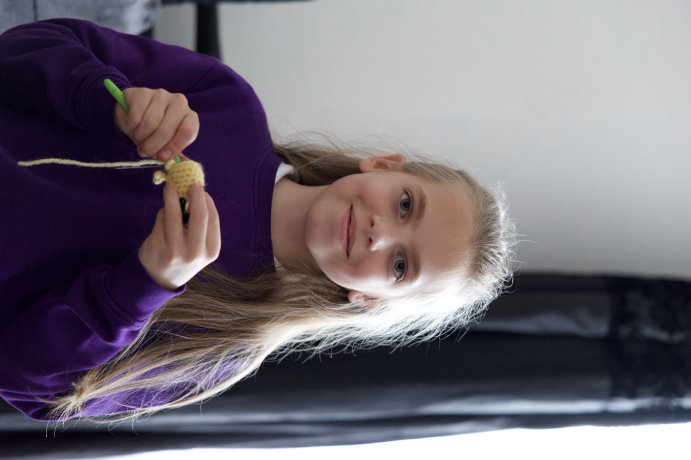 Elisa holding a crochet hook and a small yellow crochet piece she's working on
