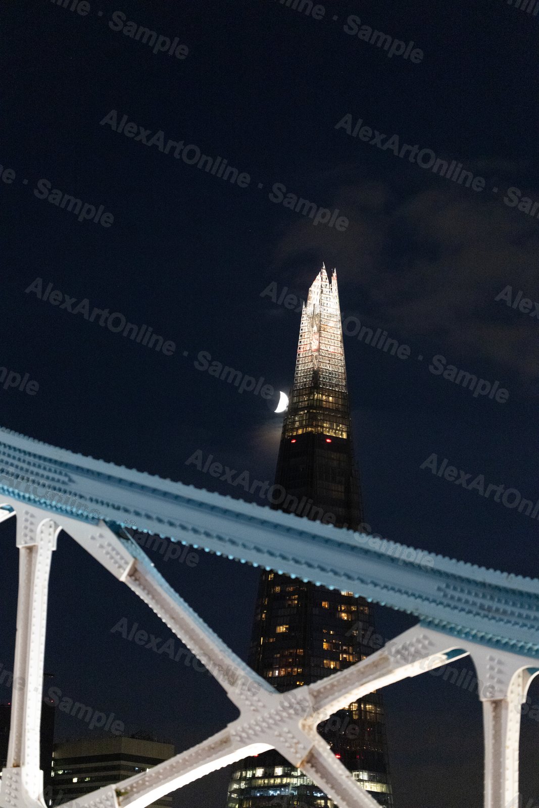 The Shard skyscraper lit at night beside a rising moon, framed through Tower Bridge's ironwork